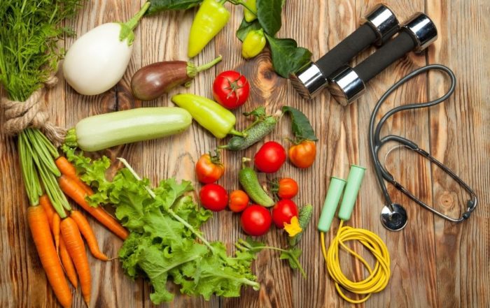 Obst, Gemüse, Hanteln und ein Stetoskop liegen auf einer Holzplatte