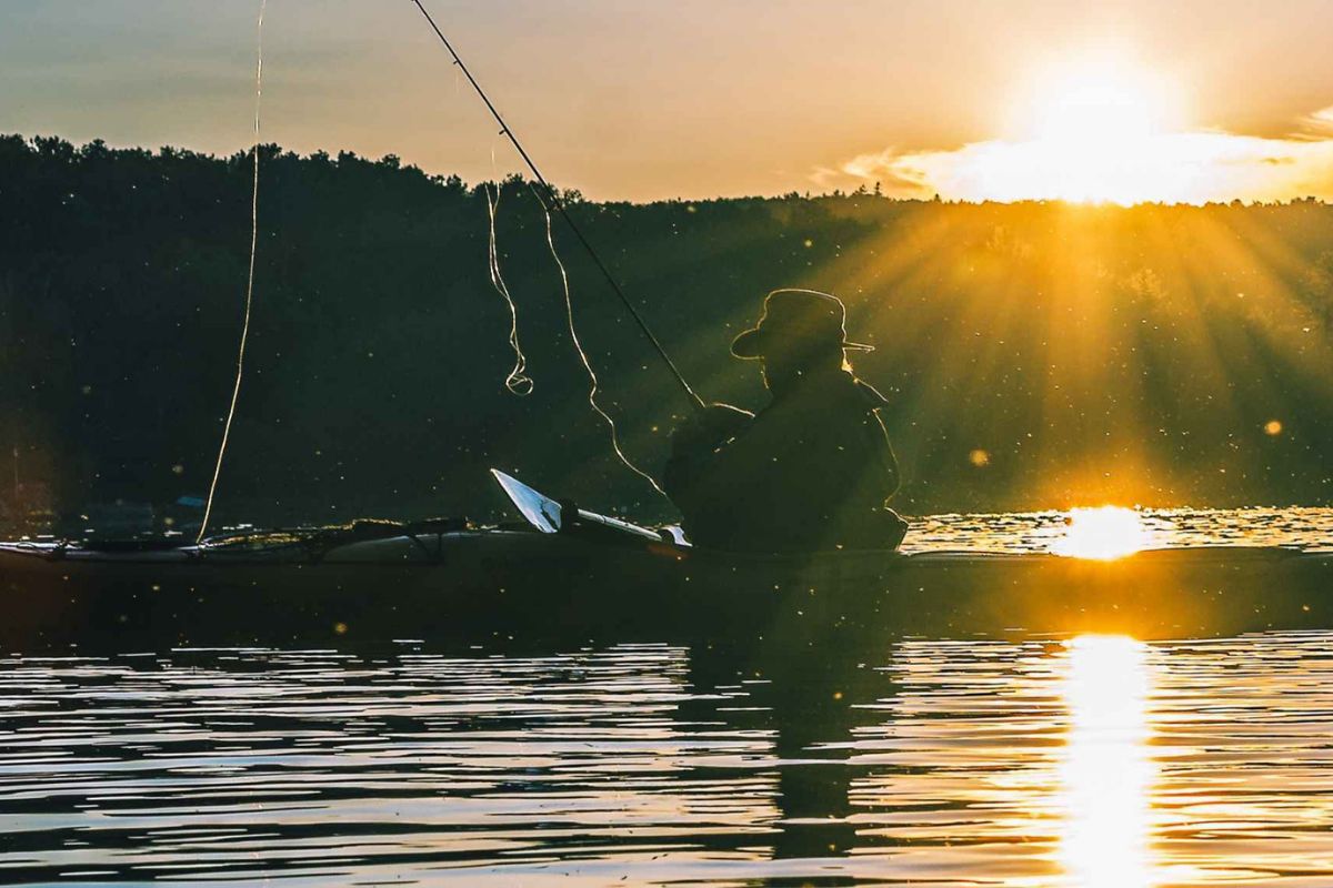 Eine Person sitzt beim Sonnenuntergang in einem Boot und fischt etwas aus dem Wasser