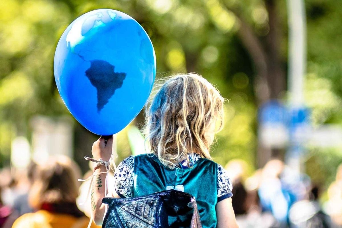 Ein Kind hält einen Blauen Luftballon mit einer Weltkugel darauf.