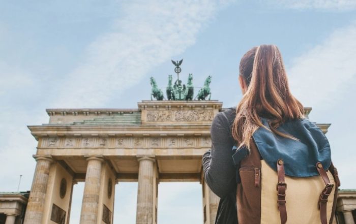 Man sieht eine blonde Frau von hinten vor dem Brandenburger Tor. Sie hat einen Rucksack auf und macht ein FÖJ in Berlin.