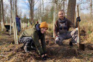 Auf dem Foto sind zwei Personen, die in der Natur Bäume pflanzen.