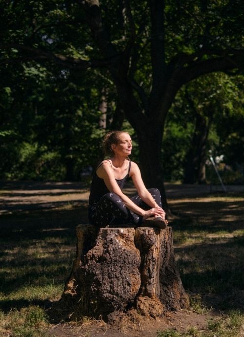 Auf dem Foto ist Gesa von Deutschland Forstet Auf zu sehen. Sie sitzt im Wald im Schneidersitz auf einem Baumstumpf und hat die Augen geschlossen. Die Sonne strahlt ihr ins Gesicht. Gesa will den Wald retten.