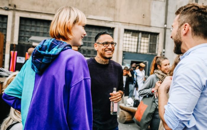 Auf dem Bild sieht man drei Personen, die sich unterhalten. Zwei stehen mit dem Rücken zur Kamera. Alle sind am lächeln und befinden sich im Machwerk in Berlin. Rechts ist einer der Gründer von GoNature, Malte Bedürftig, zu sehen.