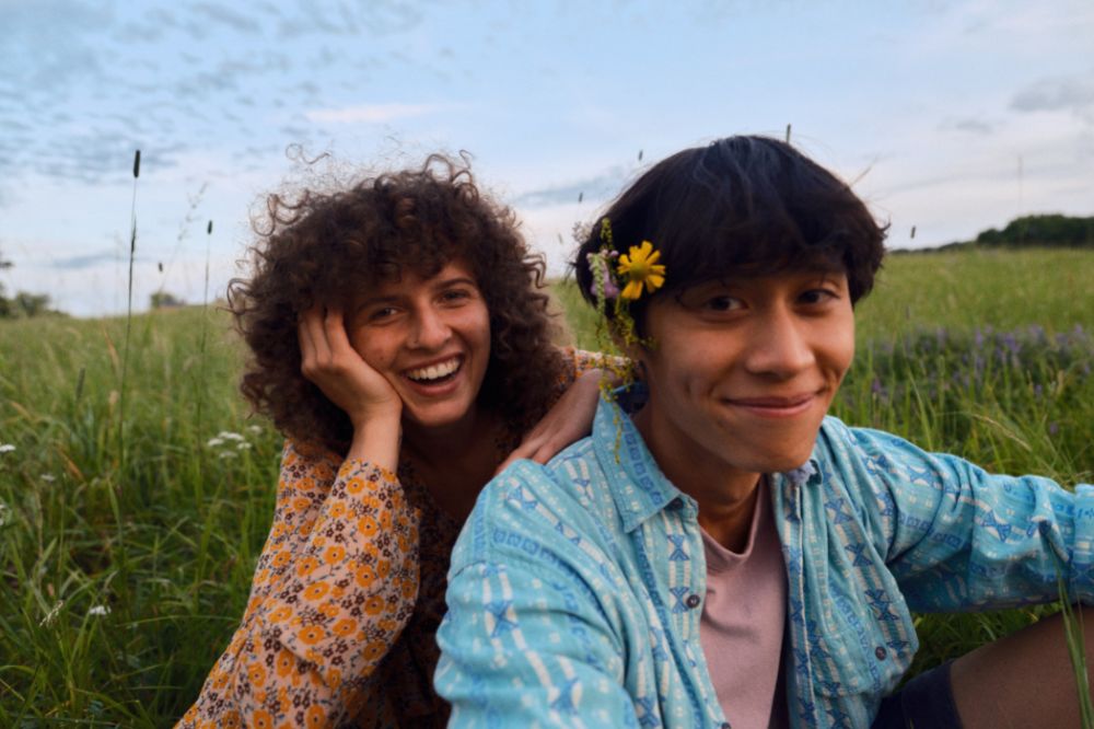 2 junge Menschen sitzen in der Natur und lachen in die Kamera. Beitragsbild für Artikel "Nachhaltige Aktivitäten im Frühling"